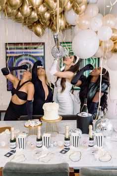 three women standing in front of a table with cake and balloons on top of it