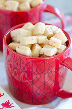 two red mugs filled with marshmallows on top of a white table