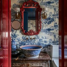 a bathroom with blue and white wallpaper, red vanity mirror and bowl on the counter