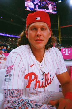 a baseball player sitting in front of a crowd at a game wearing a red hat