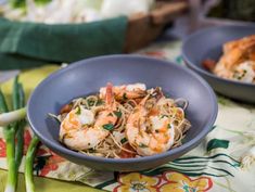 two bowls filled with shrimp and noodles on top of a table cloth next to green onions