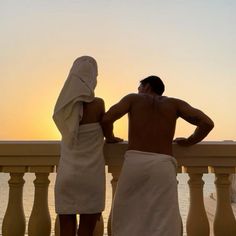 two people standing on a balcony looking out at the ocean with towels wrapped around them