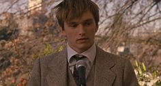 a young man wearing a suit and tie holding a microphone in front of him while standing next to flowers