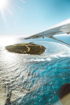 an airplane wing flying over the ocean with a small island in the middle of it