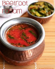 two bowls of food sitting on top of a wooden table next to silver spoons