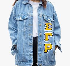 a person wearing a jean jacket with letters on the front and back, standing in front of a white background