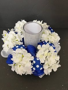 a blue vase filled with white flowers on top of a black table next to a candle