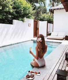 a woman sitting on the edge of a swimming pool with donuts in front of her