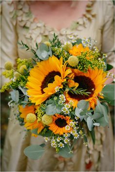 a bride holding a bouquet of sunflowers and greenery