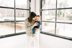 a woman holding a baby in front of a window