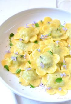 a white plate topped with pasta covered in yellow sauce and purple flowered garnish