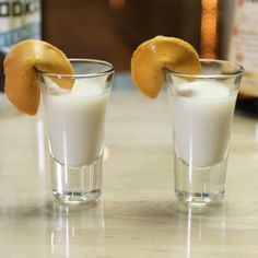 two shot glasses filled with white liquid and orange peels on top of a counter