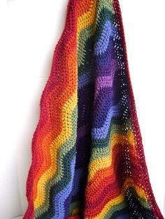 a multicolored crocheted blanket hanging from a hook on a white wall