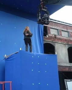 a woman standing on top of a blue box in front of a camera set up