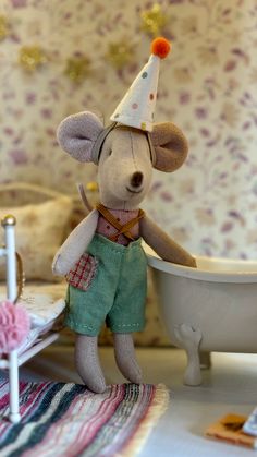 a toy mouse with a party hat and green shorts in front of a bathtub