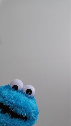 a blue stuffed animal with big eyes standing in front of a white wall and looking at the camera