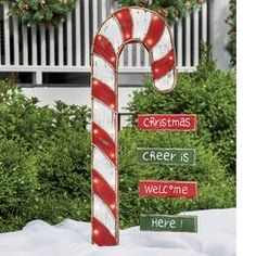 a large candy cane with christmas signs on it's side in front of some bushes