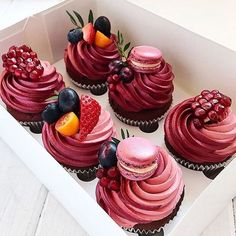 the cupcakes are decorated with pink icing and fruit on top, along with berries