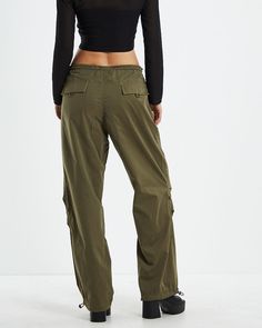 The Effie Utility Parachute Pants by Neon Hart are a parachute-style pant that comes in a khaki green colourway. The pants are designed with a durable polyester blend fabrication and are a relaxed fit. Featuring a low rise design, two front pockets with velcro closure, adjustable elasticated drawstring waist with toggles, adjustable drawstring ankle toggles and two back pockets with velcro closure. Style it with a black cropped tank and platform boots for a grungy street look.Our model is wearing a size small. She is 179cm tall with a 88cm bust, a 70cm waist and 89cm hips. Cargo Parachute Pants, Teen Shopping, Destination Dress, Style Pant, Black Cropped Tank, Skirt Jumpsuit, Street Look, Skirted Swimwear, Khaki Green