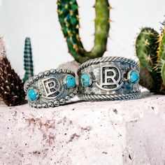 This handsome Gentlemen Cattle Brand Ring, made with sterling silver, adds the perfect touch of western style to any ensemble. The detailed craftsmanship of this classic ring showcases the brand with our design and artisan flare. A must-have for any modern-day cowboy. Features: 13mm wide in front 4mm wide on back Solid sterling silver .925 2 Kingman turquoise stone optional Customizable with brand or initial Hammered texture with rope border Handmade in PA Made to order allow 2 to 4 weeks for pr Adjustable Sterling Silver Turquoise Ring In Western Style, Western Sterling Silver Turquoise Concho Ring, Adjustable Western Turquoise Concho Ring, Western Sterling Silver Concho Rings, Western Style Sterling Silver Concho Rings, Western Sterling Silver Turquoise Ring, Ring Initials, Cattle Brands, Rope Border