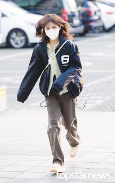 a woman wearing a face mask walking down the street with her hands in her pockets