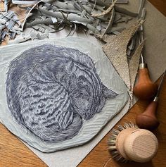 a cat sitting on top of a piece of paper next to some scissors and thread