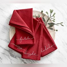 red towels with embroidered names on them sitting on a white marble counter top next to evergreen branches