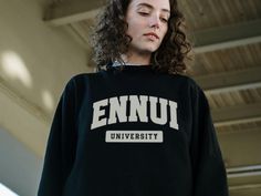 Feeling listless and dissatisfied with the world? Join the club at Ennui University! This cozy, light-weight crewneck sweatshirt features a bold, collegiate-style graphic across the chest that says "Ennui University" - a playful nod to the existential crisis we're all experiencing. Crafted from soft 100% ringspun cotton, it's the perfect comfy-yet-stylish way to embrace your ennui with a wink and a smile. Whether you're a disillusioned college student or just someone who was promised the American Dream but got crushed under the weight of capitalism, this sweatshirt lets you wear your angst on your sleeve (literally) while maintaining a sense of humor. Machine washable and built to last, it's a cozy reminder that we're all in this together, even if life feels a bit aimless sometimes. Produc Crew Neck T-shirt With University Logo For Fall, University Logo Long Sleeve Tops For Sports Season, Long Sleeve University Logo Tops For Sports Season, Long Sleeve Tops With University Logo For Sports Season, Sporty University Logo Tops For Streetwear, Sporty Streetwear Tops With University Logo, Varsity Logo Print Sweatshirt For Campus, University Logo Long Sleeve Tops For Streetwear, Sporty Crew Neck Sweats For Campus