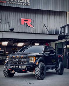 a large black truck parked in front of a building with the name r on it