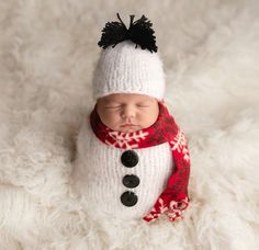 a newborn baby wearing a snowman hat and scarf is sleeping on a fluffy white blanket