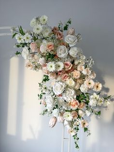 an arrangement of white and pink flowers in a vase on a stand against a wall