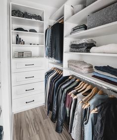 a walk in closet with white shelving and lots of clothes