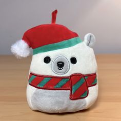 a white stuffed bear wearing a red and green christmas hat on top of a wooden table