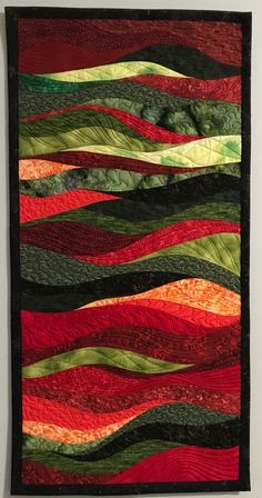 a quilted wall hanging on the side of a white wall with red, green and orange stripes