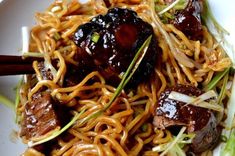 a white plate topped with noodles and meat covered in gravy next to chopsticks