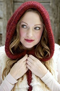 a woman wearing a red hat and scarf with her hands under her face while standing in front of a wooden wall