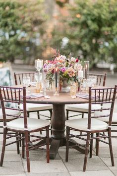 the table is set with white chairs and flowers in vases, candles, and wine glasses