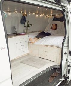 a woman laying on top of a bed in the back of a white van with its doors open