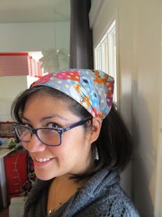 a woman wearing glasses and a bandana smiles at the camera while standing in front of a kitchen