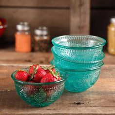 three glass bowls filled with strawberries on top of a wooden table next to jars