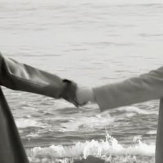 two people holding hands while standing in front of the ocean