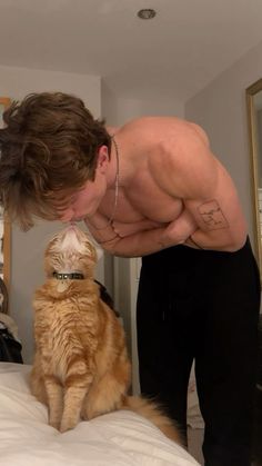 a man kissing a cat on the nose while standing on top of a white bed