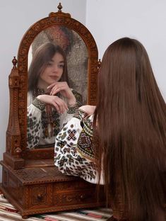 a woman is looking at her reflection in the mirror while she brushes her long hair