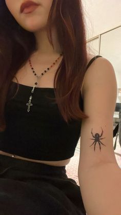 a woman with a spider tattoo on her left arm and cross tattooed on the right arm