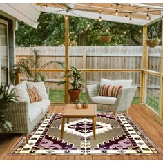 an outdoor living area with couches, chairs and a rug on the ground in front of a wooden fence