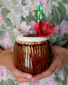 a person holding a vase with flowers in it and two bamboo sticks sticking out of the top