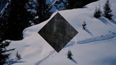 a black diamond shaped sign in the middle of some snow covered ground with evergreen trees behind it