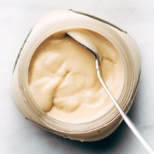 a jar filled with mayonnaise sitting on top of a white counter next to a spoon