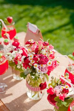 red flowers in vases are sitting on a table with wine glasses and napkins