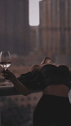 a woman holding a glass of wine on top of a roof in front of buildings